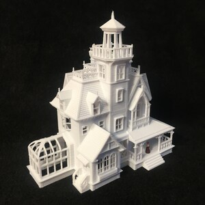 May include: A white 3D printed model of a Victorian style house with a greenhouse and a small figure standing on the porch.
