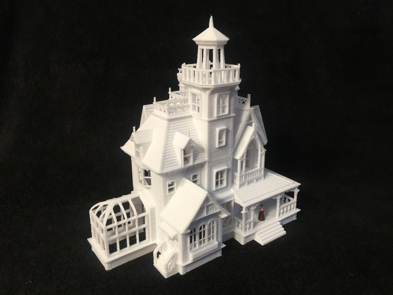 May include: A white 3D printed model of a Victorian style house with a greenhouse and a small figure standing on the porch.
