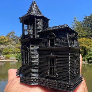 May include: A black 3D printed model of a Victorian-style house with a tower, multiple windows, and a brick foundation.