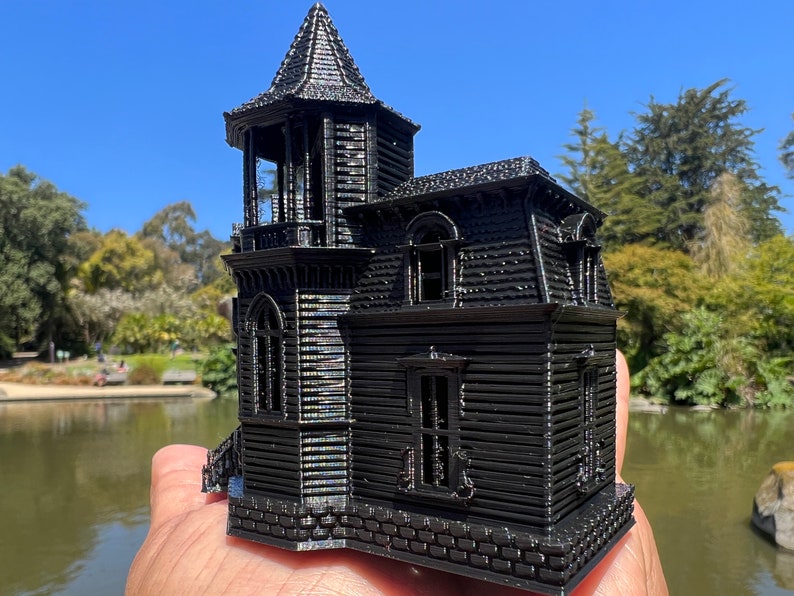 May include: A black 3D printed model of a Victorian-style house with a tower, multiple windows, and a brick foundation.