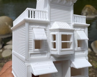May include: A white 3D printed model of a two-story building with a storefront, windows, and a balcony. The building has a detailed facade with decorative trim and awnings.