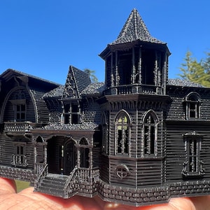 May include: A black 3D printed model of a Victorian style house with intricate details, including a tower, windows, and a porch.