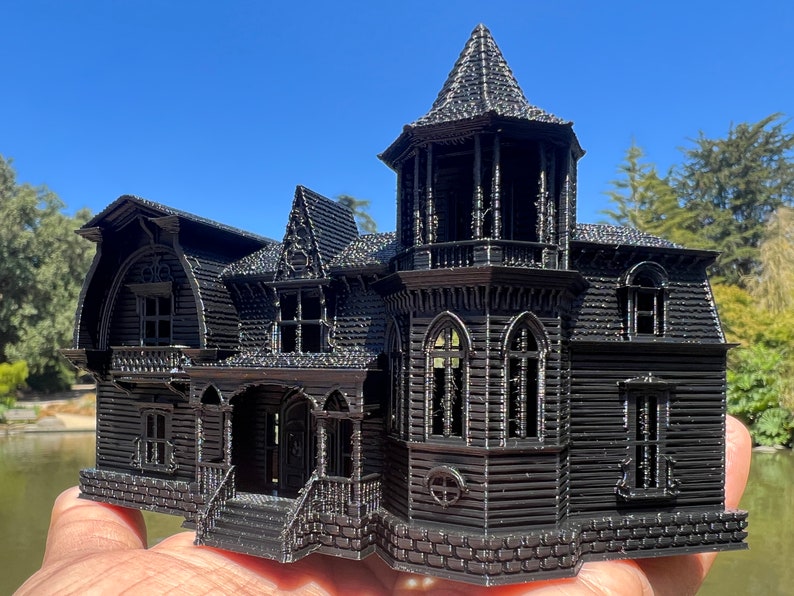 May include: A black 3D printed model of a Victorian style house with intricate details, including a tower, windows, and a porch.