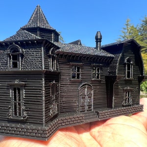 May include: A black 3D printed model of a haunted house with a pointed roof, multiple windows, and a brick foundation.