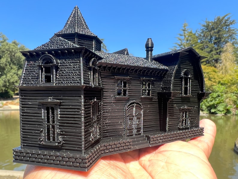 May include: A black 3D printed model of a haunted house with a pointed roof, multiple windows, and a brick foundation.