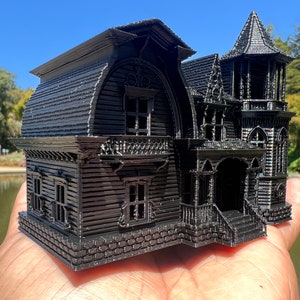 May include: A black 3D printed model of a Victorian style house with a steep roof, multiple windows, and a front porch. The model is detailed with intricate trim and brickwork.