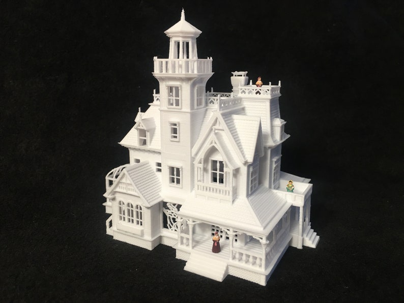 May include: A white 3D printed model of a Victorian-style house with a tower, multiple windows, and a porch. There are small figures of people standing on the porch and roof.