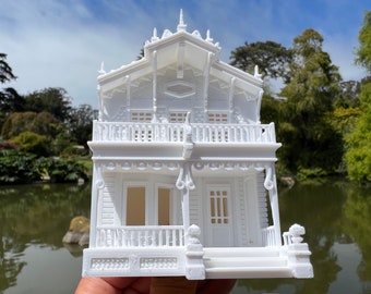 May include: A white 3D printed model of a Victorian style house with intricate details, including a balcony, porch, and windows.