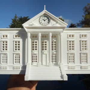 May include: White 3D printed model of a building with a clock tower and a front entrance with steps. The building has a brick pattern and windows.
