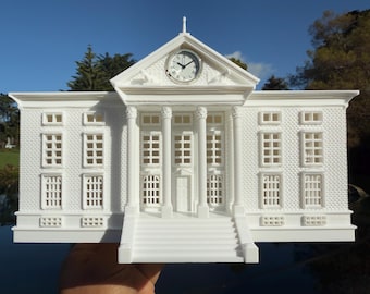May include: White 3D printed model of a building with a clock tower and a front entrance with steps. The building has a brick pattern and windows.