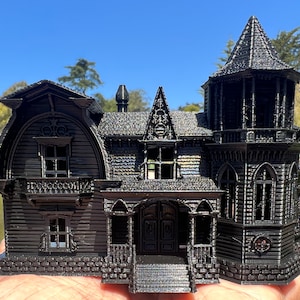 May include: A black 3D printed model of a gothic-style house with a tower, multiple windows, and a front porch. The house is detailed with intricate trim and a brick foundation.