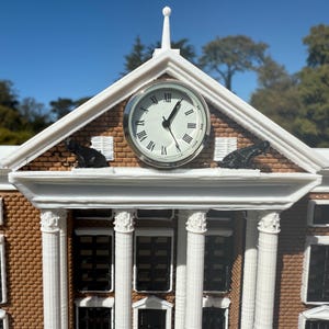 May include: A white model of a building with a clock tower. The clock face has black Roman numerals and hands. There are two black cat figurines on the roof.