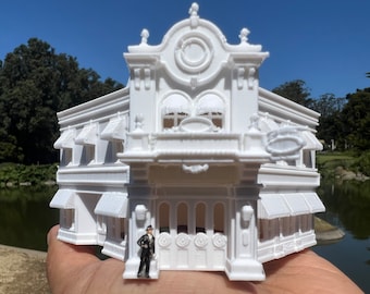 May include: A white 3D printed model of a building with a rounded roof and ornate details. The building has multiple windows and a sign that reads "The Bakery".