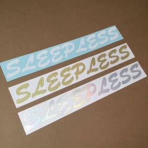 May include: Three vinyl stickers with the word "Sleepless" written in different colours and fonts. The top sticker is light blue, the middle sticker is gold, and the bottom sticker is a light purple.