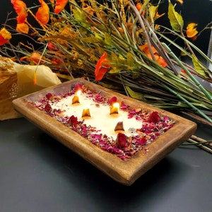 May include: A wooden tray with a white candle and dried rose petals. The candle has four wicks and is lit.