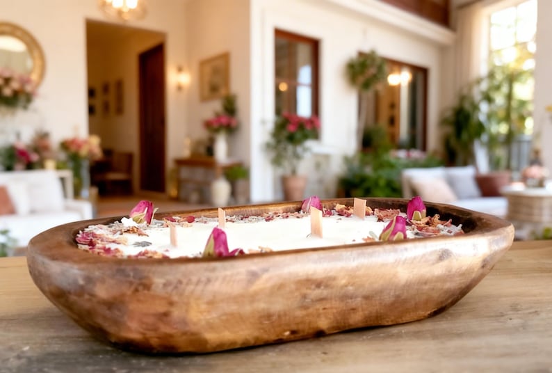 May include: A wooden candle holder filled with white wax, rose petals, and pink rose buds. The candle has several wooden wicks. The wooden bowl is oval-shaped and sits on a wooden surface. The candle is a decorative home decor item.