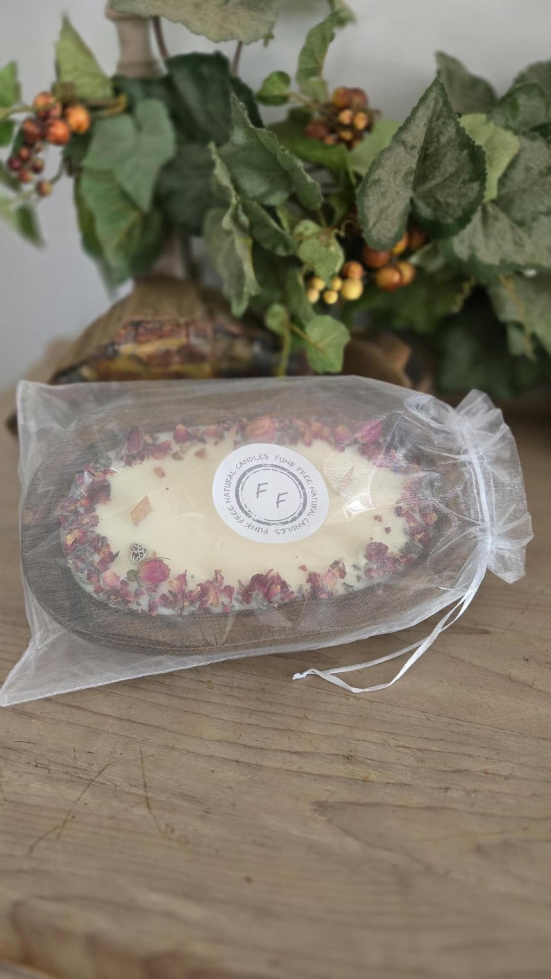 May include: A handmade candle in a wooden oval bowl, surrounded by dried rose petals. The candle is white with two wooden wicks and a circular sticker that reads "Funk Free Natural Candles". The candle is packaged in a sheer white bag.