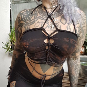 Könnte beinhalten: Schwarzes Haltertop und passender Rock. Das Oberteil hat ein einzigartiges geflochtenes Design und Used-Akzente. Der Rock hat einen hohen Schlitz an der Seite. Das Outfit ist dunkel und kreiert einen kühnen und kantigen Look. Geeignet für verschiedene Anlässe.