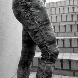 Könnte beinhalten: Grau-melierten Leggings mit Distressed-Details. Die Leggings haben mehrere Ausschnitte entlang der Beine, die durch ein geflochtenes Design verbunden sind. Die Leggings werden mit schwarzen Stiefeln getragen.