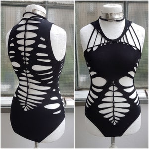 Peut inclure: Body noir avec un design découpé unique en forme de squelette. Le vêtement sans manches présente un col montant et une silhouette ajustée. Les découpes créent un effet visuel saisissant, parfait pour la mode alternative.