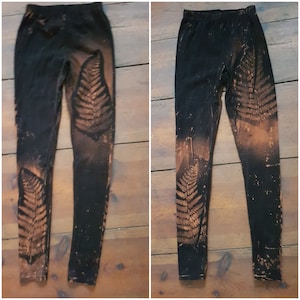 May include: Black leggings with a brown fern leaf pattern. The leggings are made of a soft, stretchy fabric.
