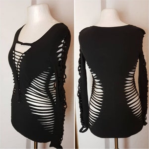 Könnte beinhalten: Schwarzes Langarm-Shirt mit einem Used-Look-Design mit mehreren vertikalen und horizontalen Schlitzen im gesamten Stoff. Das Shirt hat einen runden Ausschnitt und eine figurbetonte Silhouette.
