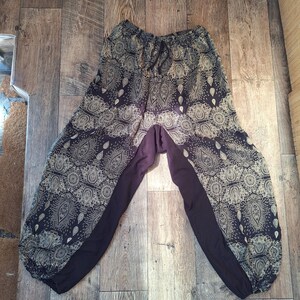 May include: A pair of harem pants with a paisley pattern in beige and dark blue. The pants have a drawstring waist and solid dark blue panels on the sides. The pants are made of a lightweight fabric.