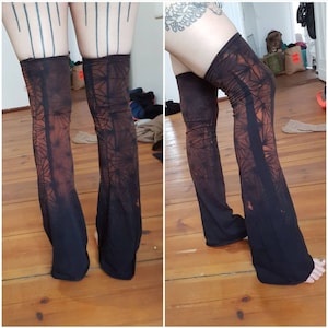 Puede incluir: Un par de polainas negras con un patrón de tie-dye naranja y marrón. Las polainas están hechas de un tejido elástico y tienen una forma acampanada.