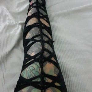 Puede incluir: Leggings negros con un diseño calado único. Los leggings presentan una serie de tiras de tela entrecruzadas que crean un patrón abierto en forma de celosía. El diseño revela la piel y los tatuajes que hay debajo. Los leggings están hechos de un material suave y elástico.