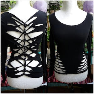 Könnte beinhalten: Schwarzes Langarmshirt mit einem einzigartigen Design mit Ausschnitten und einem Kreuzmuster auf dem Rücken.