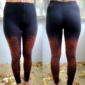 Könnte beinhalten: Schwarze Leggings mit einem einzigartigen Design. Die Leggings haben ein braunes, schuppenartiges Muster, das in den schwarzen Stoff übergeht. Das Design bedeckt den unteren Teil der Leggings und erzeugt einen unverwechselbaren Look.