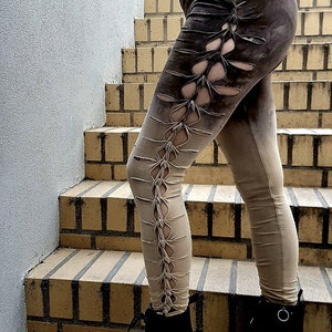 May include: Leggings featuring a dark brown to light beige gradient colour scheme. The side of the leggings displays a vertical row of cutouts held together by knotted fabric strips. The leggings are paired with black lace-up ankle boots.