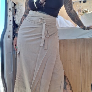 Könnte beinhalten: Ein beiger Wickelrock mit Bindeband. Der Rock ist aus leichtem Stoff gefertigt und hat eine lockere Passform. Dazu wird ein schwarzes Crop-Top getragen.