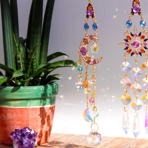 May include: Two gold-tone earrings with crystal accents. One earring features a crescent moon with purple and blue crystals. The other earring features a star with orange, pink, and blue crystals.