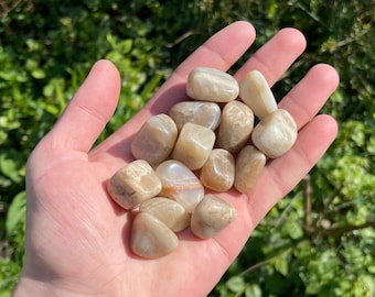 May include: A collection of tumbled sunstone stones in various shades of beige and brown. The stones are smooth and polished, with a slight shimmer.