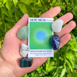 May include: A set of five crystals for new mothers, including blue tiger's eye, howlite, light aventurine, sodalite, and snow quartz. The crystals are arranged on a hand with a card that reads "NEW MUM - CRYSTALS FOR NEW MUMS".