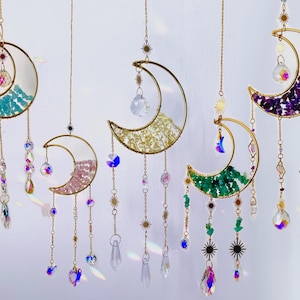 Peut inclure: Plusieurs attrape-soleil en forme de croissant de lune avec des cadres dorés et des perles et cristaux de différentes couleurs. Chaque lune a une palette de couleurs différente, notamment le bleu, le rose, le jaune, le vert et le violet. Les attrape-soleil sont suspendus à des chaînes délicates.