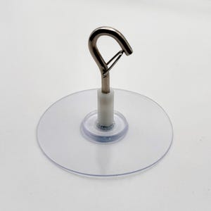 May include: Clear suction cup with a metal hook. The hook is silver and has a curved design. The suction cup is round and transparent, with a white stem connecting it to the hook. Ideal for hanging items on smooth surfaces.