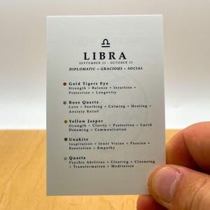 May include: A white card with the astrological sign Libra and the text "SEPTEMBER 23 - OCTOBER 22" and "DIPLOMATIC - GRACIOUS - SOCIAL". The card lists five crystals associated with Libra: Gold Tiger's Eye, Rose Quartz, Yellow Jasper, Unakite, and Quartz. Each crystal is listed with its properties.