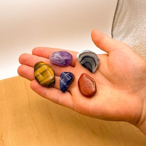 Peut inclure: Une collection de six pierres roul&eacute;es de diff&eacute;rentes couleurs, dont l'am&eacute;thyste violette, le lapis-lazuli bleu, l'&oelig;il de tigre brun, le jaspe rouge et l'agate grise.