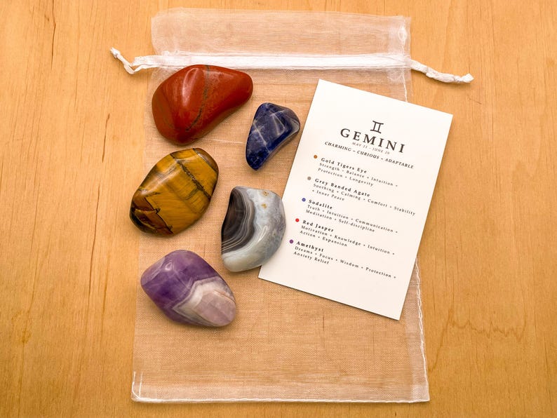 Peut inclure: Un ensemble de six pierres roul&eacute;es dans un sac en organza blanc avec une carte qui indique "G&eacute;meaux : Charmant - Curieux - Adaptable" et liste les pierres et leurs significations associ&eacute;es. Les pierres sont du jaspe rouge, de l'&oelig;il de tigre dor&eacute;, de l'agate ruban&eacute;e grise, de la sodalite, de l'am&eacute;thyste et de l'agate bleue.