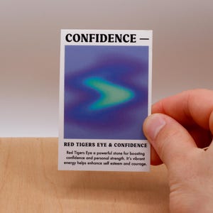 May include: A white card with the text "CONFIDENCE -" at the top and "RED TIGERS EYE & CONFIDENCE" at the bottom. The card has a blue and green gradient image in the center. The text below the image reads: "Red Tigers Eye a powerful stone for boasting confidence and personal strength. It's vibrant energy helps enhance self esteem and courage."