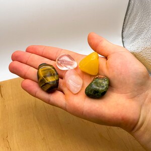 May include: A collection of five tumbled stones, including clear quartz, rose quartz, tiger's eye, aventurine, and citrine.