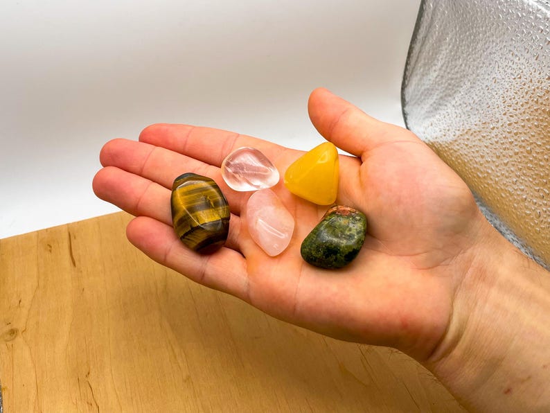 May include: A collection of five tumbled stones, including clear quartz, rose quartz, tiger's eye, aventurine, and citrine.