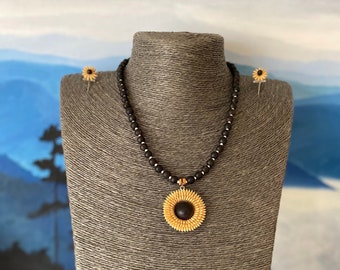 May include: A black beaded necklace with a sunflower pendant and matching sunflower earrings. The necklace and earrings are made of wood and have a natural finish.