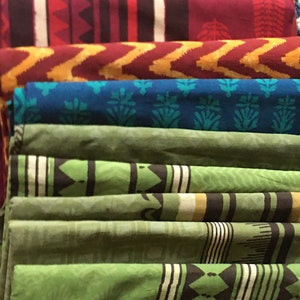 May include: A stack of colorful fabric scraps with various patterns, including stripes, zigzags, and floral designs. The fabric is folded neatly and arranged in a vertical stack.