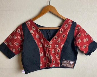May include: A red and black cotton blouse with a V-neckline and a button-up front. The blouse has a floral print and a black lace trim. The blouse is on a hanger.