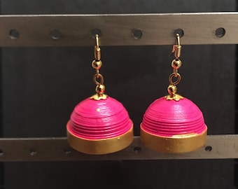 May include: A pair of pink and gold dangle earrings. The earrings are made of paper and have a dome shape. The earrings are hanging from gold hooks.