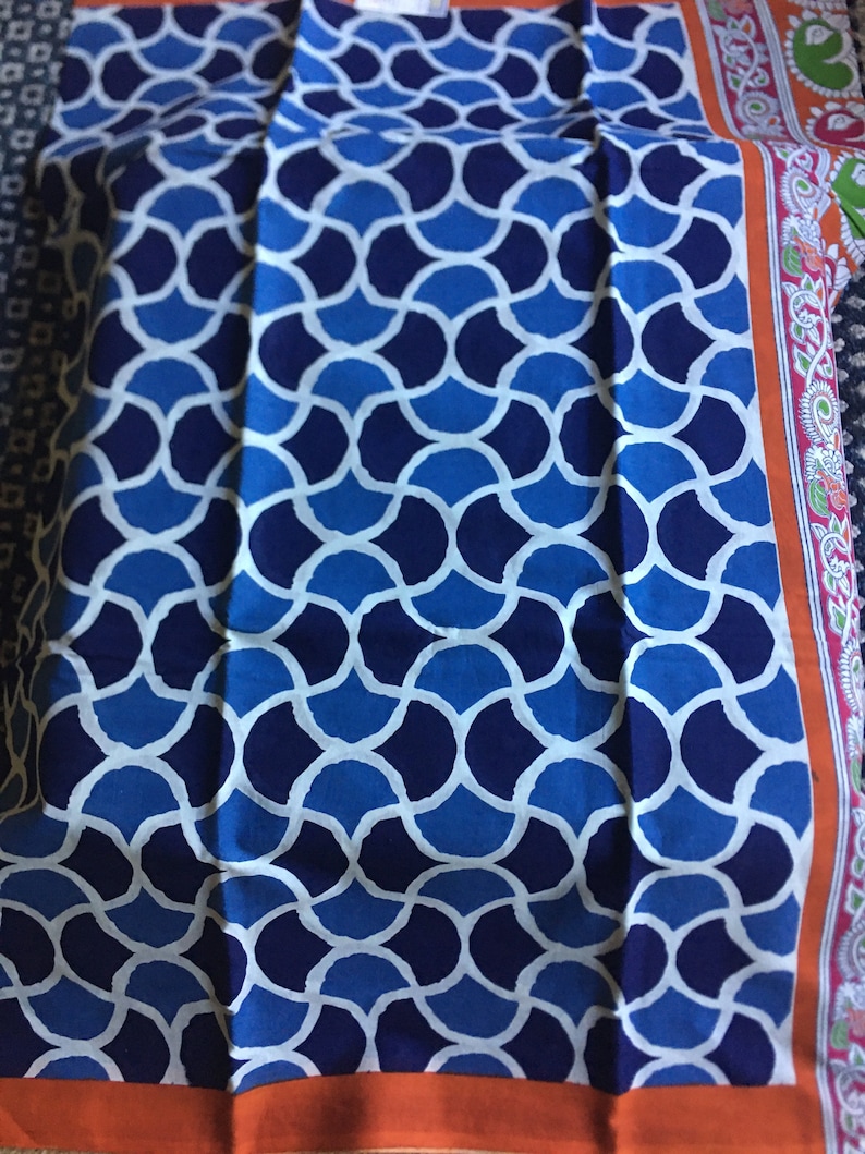 May include: A blue and white patterned fabric with a geometric design. The fabric has a dark blue border with a white and orange trim.