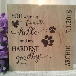 May include: A wooden plaque with the text "YOU were my favorite hello and my HARDEST goodbye" with a heart and paw prints. The plaque also includes the name "ARCHIE" and the date "7.1.2018".